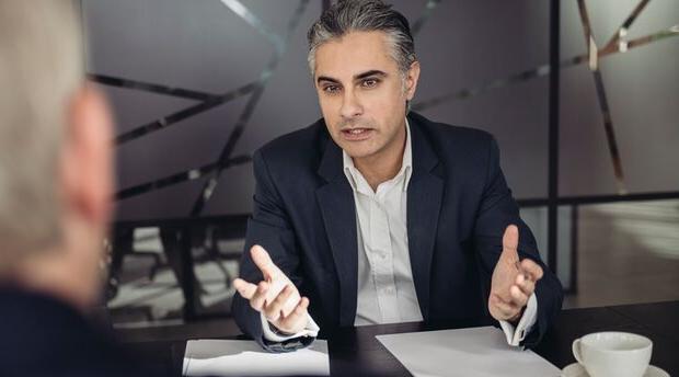 Two colleagues seated at a table engaging in conversation with a colleague standing nearby